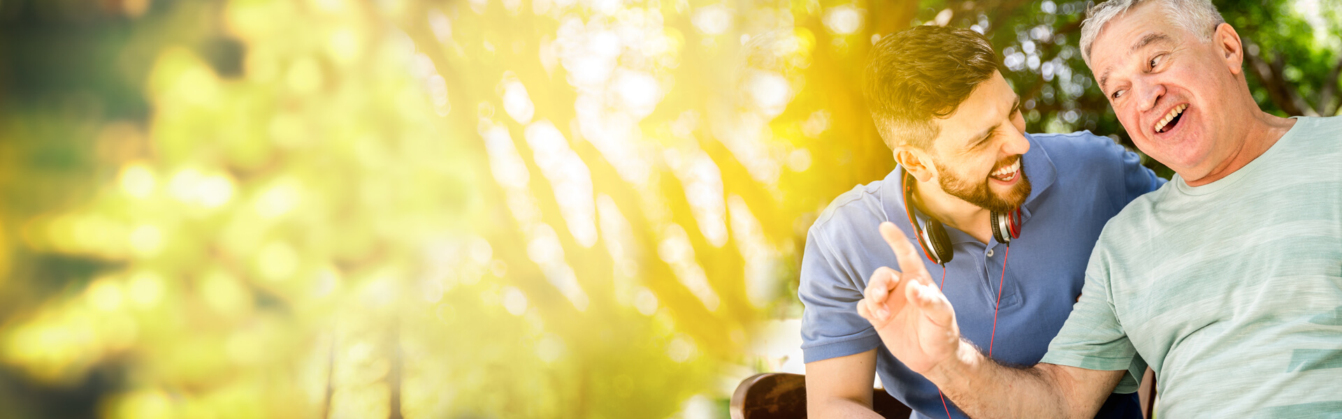 Crédito de Libranza Padre, 68 años e hijo de 35, en un momento de conversación. Se ven cercanos, están en el parque en una linda tarde. hablan de temas divertidos. El papá le cuenta que se siente tranquilo con su Crédito de Libranza.