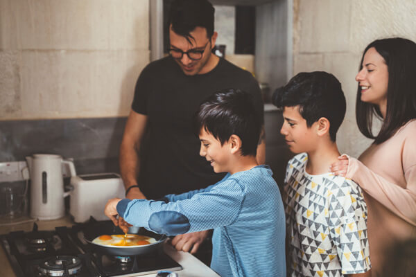 Familia feliz que comparte nuevas experiencias en la cocina, porque lograron sus sueños a través de la Cuentamiga Mi Casa, Mi Ahorro.