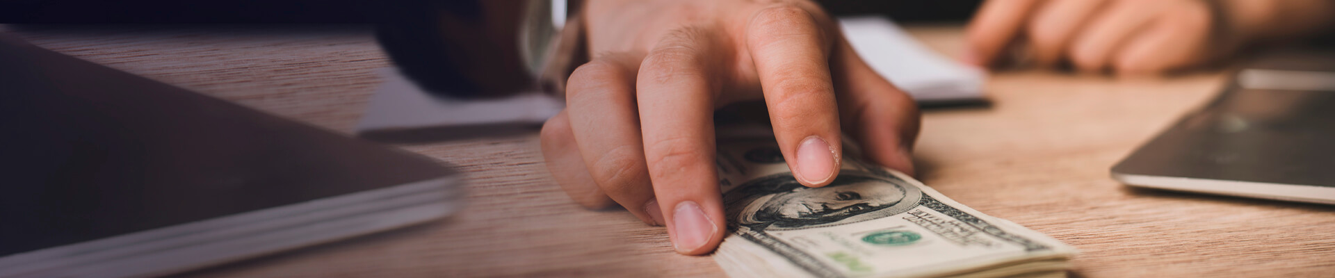 Sobre un escritorio una mano muestra un fajo de dólares. En el Banco sí cuenta con productos para realizar transacciones en moneda extranjera